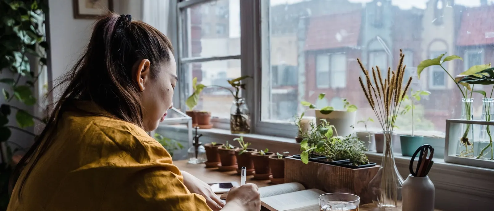 A woman writing in a notebook at a desk by the window