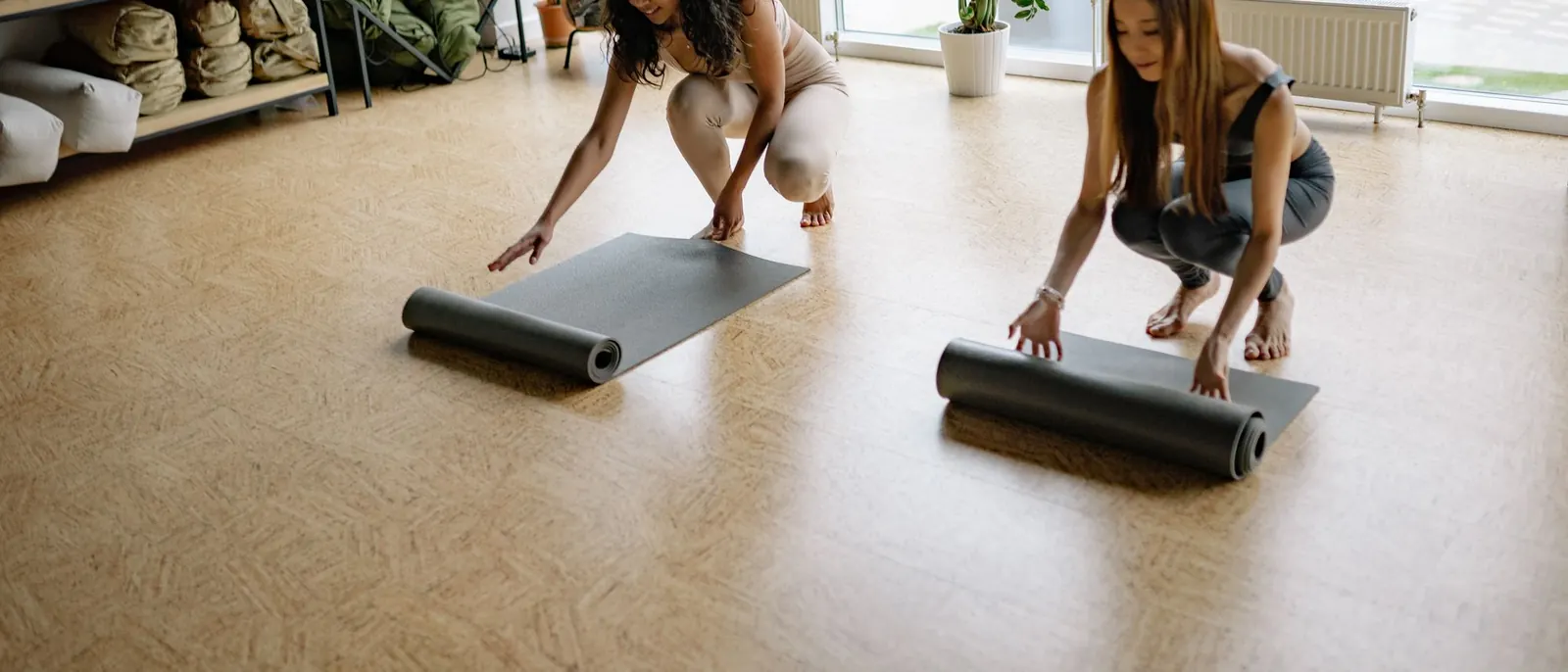 Two women unrolling their yoga mats in a sunlit studio