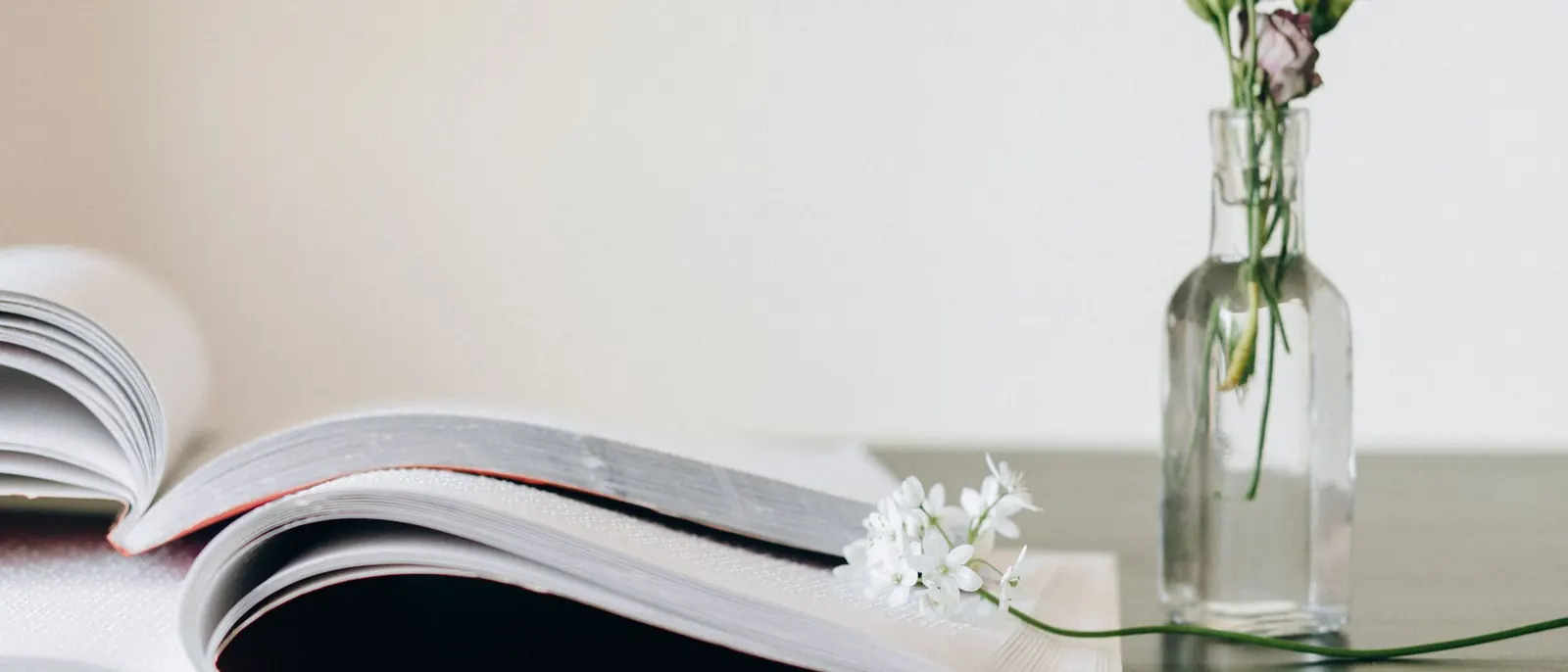An open book beside a small glass vase of flowers