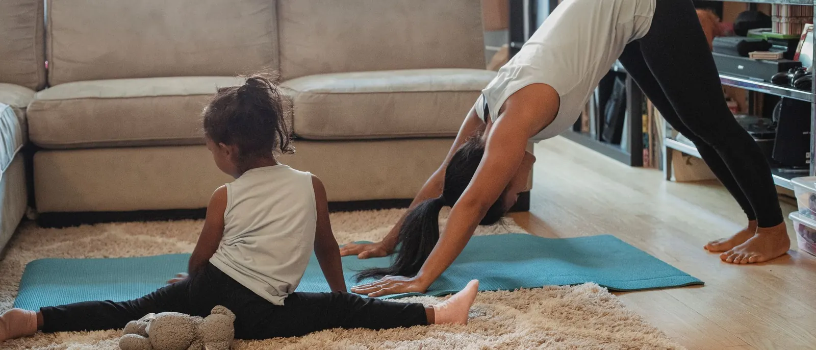 A parent in Downward-Facing Dog while a child stretches beside them in the living room